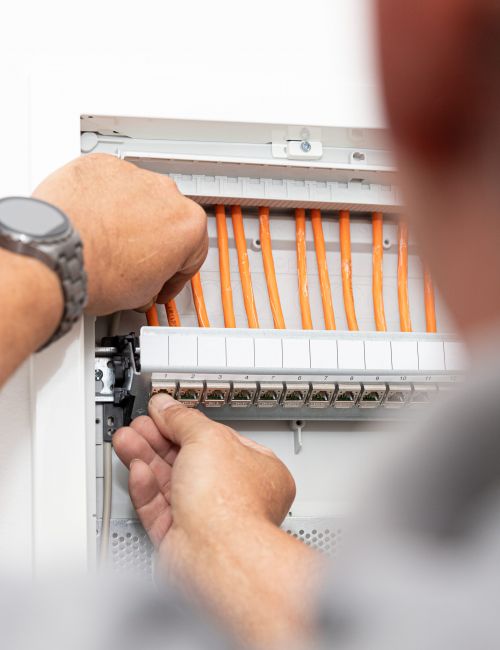 Bildausschnitt eines Elektromeisters beim anschließen von Datenkabeln im Schaltschrank.