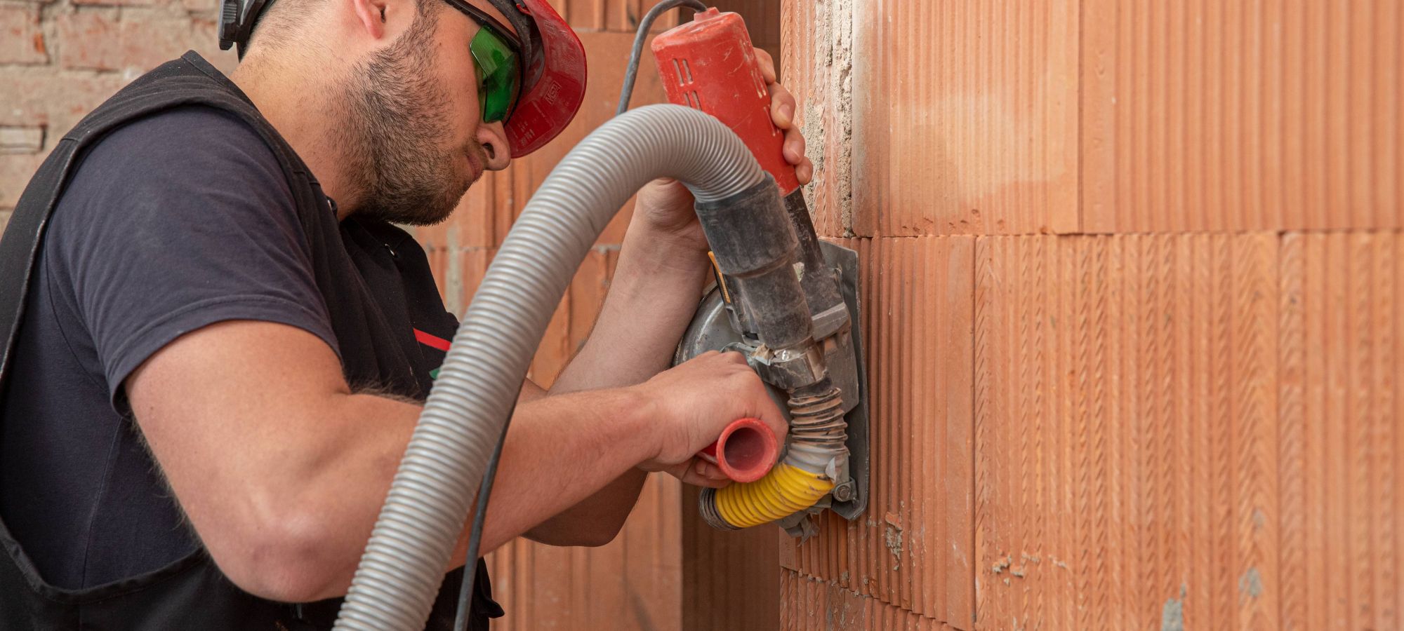 Junger Elektromonteur bei der Rohinstallation schlitzt mit Mauernutfräse in Ziegelwand