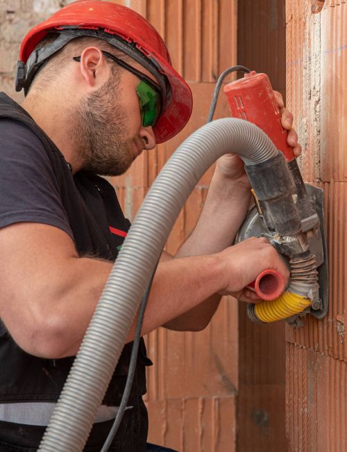 Junger Elektromonteur bei der Rohinstallation schlitzt mit Mauernutfräse in Ziegelwand