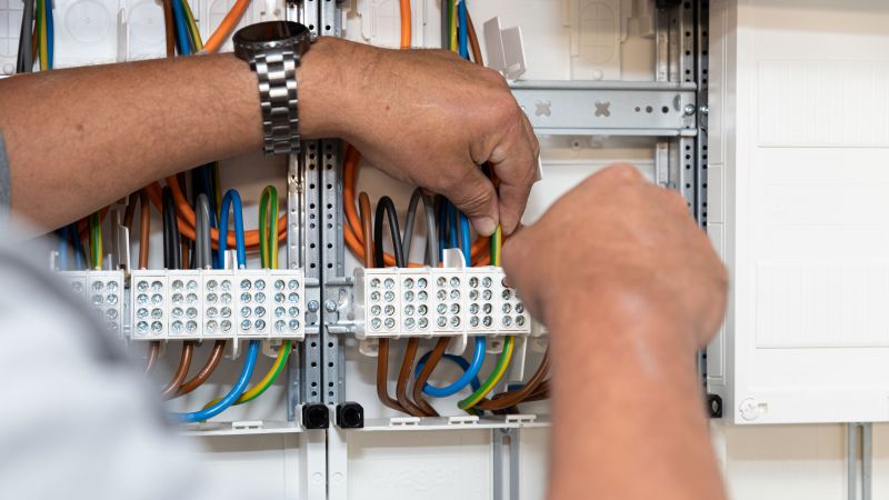Bildausschnitt mit Händen eines Elektromeisters, beim anschließen von verschiedenen Kabeln im Zählerschrank.